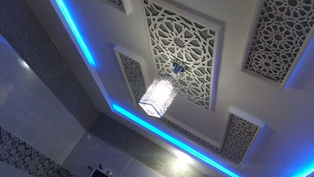 A room with a patterned ceiling, a hanging light fixture, and a small screen mounted on the wall.