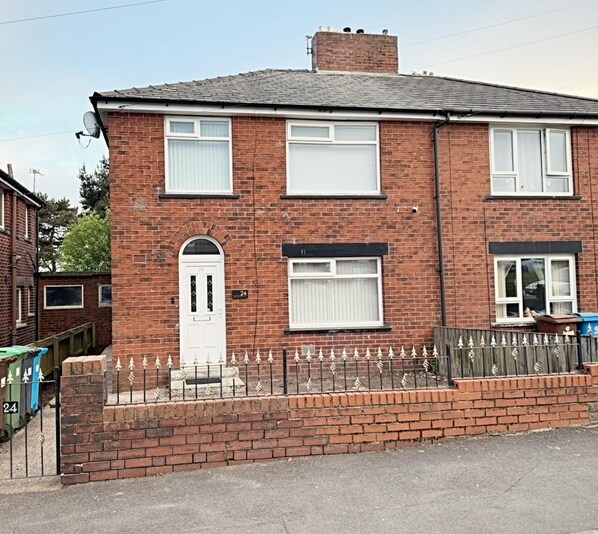 A two-story brick house with a white door and windows, a brick driveway, and a metal fence. - The Serene Stays Sleeps 6 With Garden (Oldham)