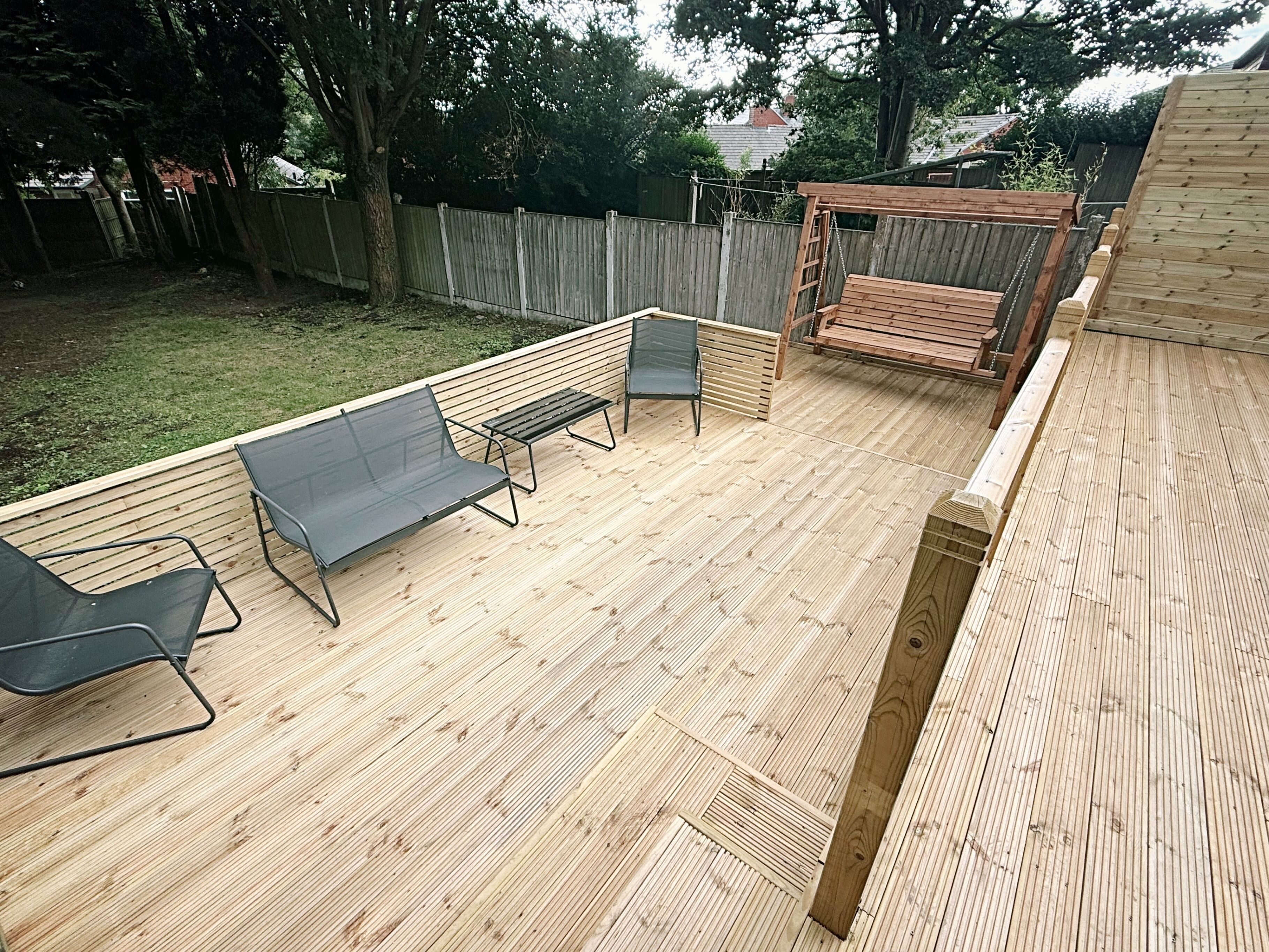 A wooden deck with outdoor furniture, including two lounge chairs and a bench.