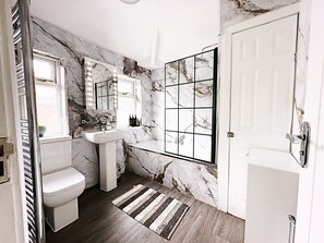 A bathroom with a marble wall, a sink, a toilet, and a shower area. - The Serene Stays Sleeps 6 With Garden (Oldham)