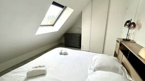 A bedroom with a skylight, a bed with white linens, a dresser, and a bedside lamp.