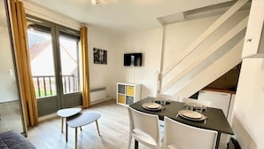 A modern room with a dining table set for two, a sofa, and a staircase leading to an upper level.