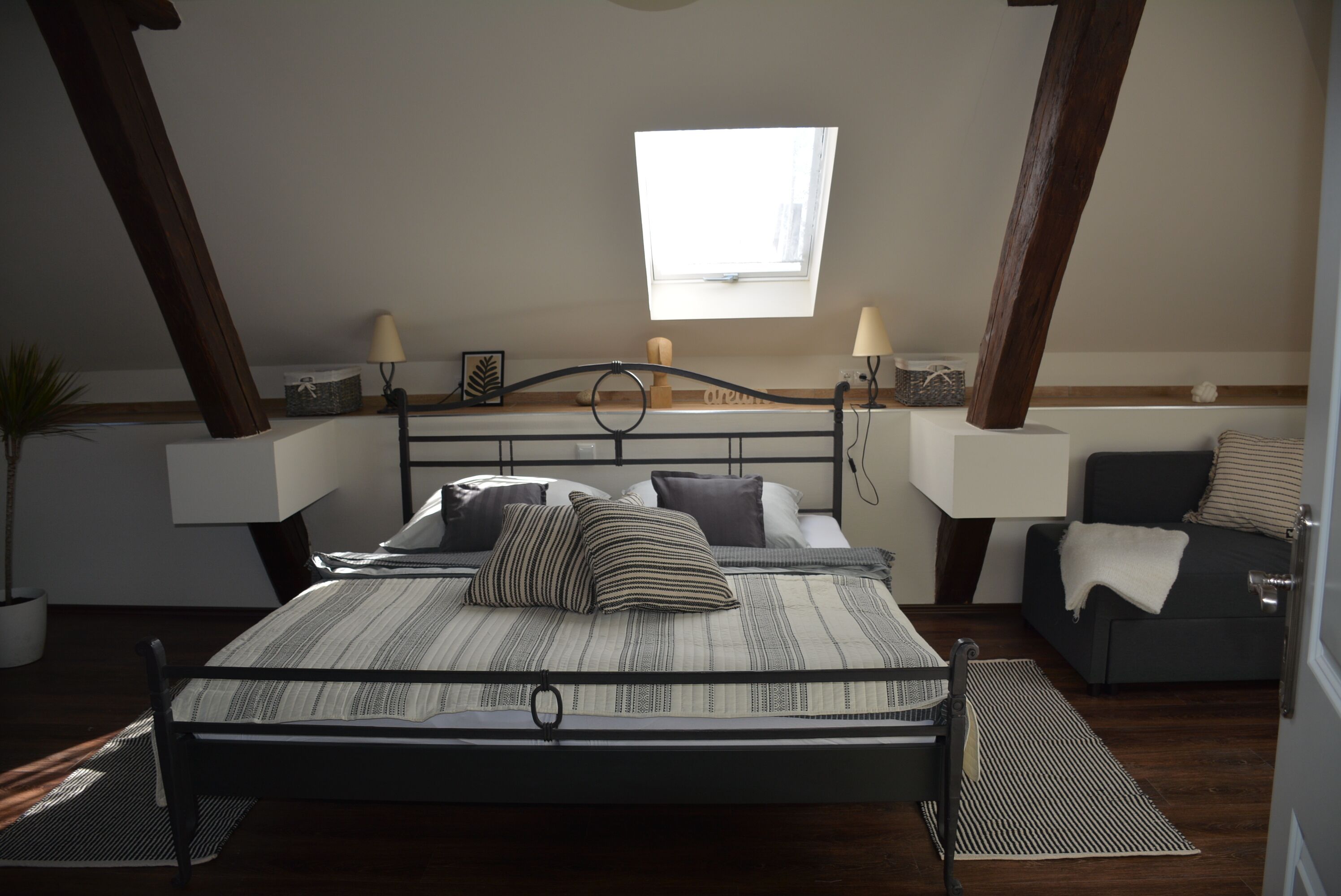 Een slaapkamer met een bed, nachtlampjes, een raam en een klein tafeltje met een lamp.