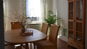 Ein Essbereich mit einem runden Holztisch, Korbstühlen, einer Vase mit Zweigen und einer Vitrine mit Glastüren.