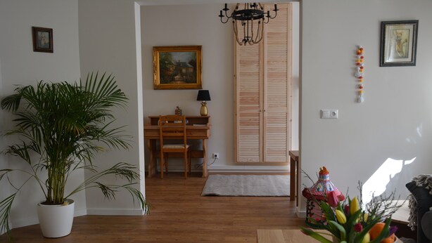 Ein Zimmer mit Holzboden, einem Esstisch mit Stühlen, einer Topfpflanze, einer Vase mit Blumen und einem Gemälde an der Wand.