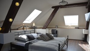 Ein Schlafzimmer im Loft-Stil mit Schräge, Dachfenstern, einem Bett mit gestreifter Bettwäsche und einem Nachttisch mit Lampe.