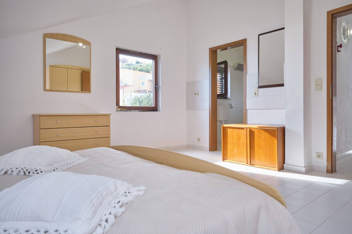 Un dormitorio con una cama, un aparador de madera, un espejo y una ventana.