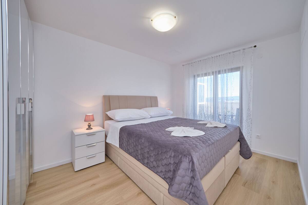 Un dormitorio con cama, mesita de noche y ventana con cortinas.