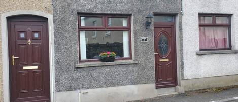 Ein zweistöckiges Gebäude mit strukturierter Fassade, nummerierten Hauseingängen und einem Fenster mit Blumenkasten.