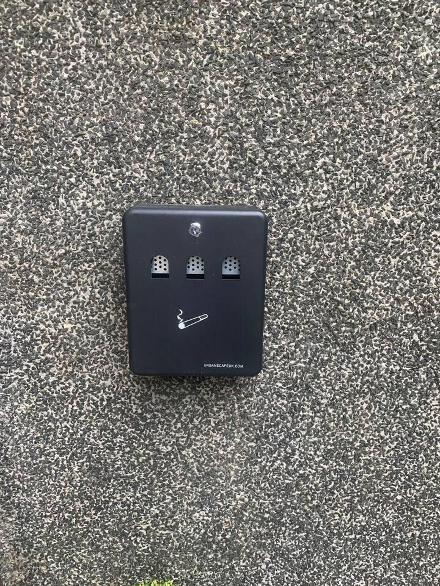 A black electrical outlet with three sockets and a cigarette butt symbol on a textured surface.