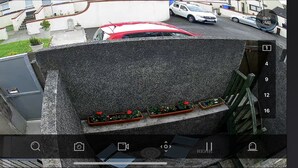 A security camera view of a residential area with a red car parked on the street, a white car in the background, and a staircase leading to a building. - Minimum Stay two Nights (Larne)