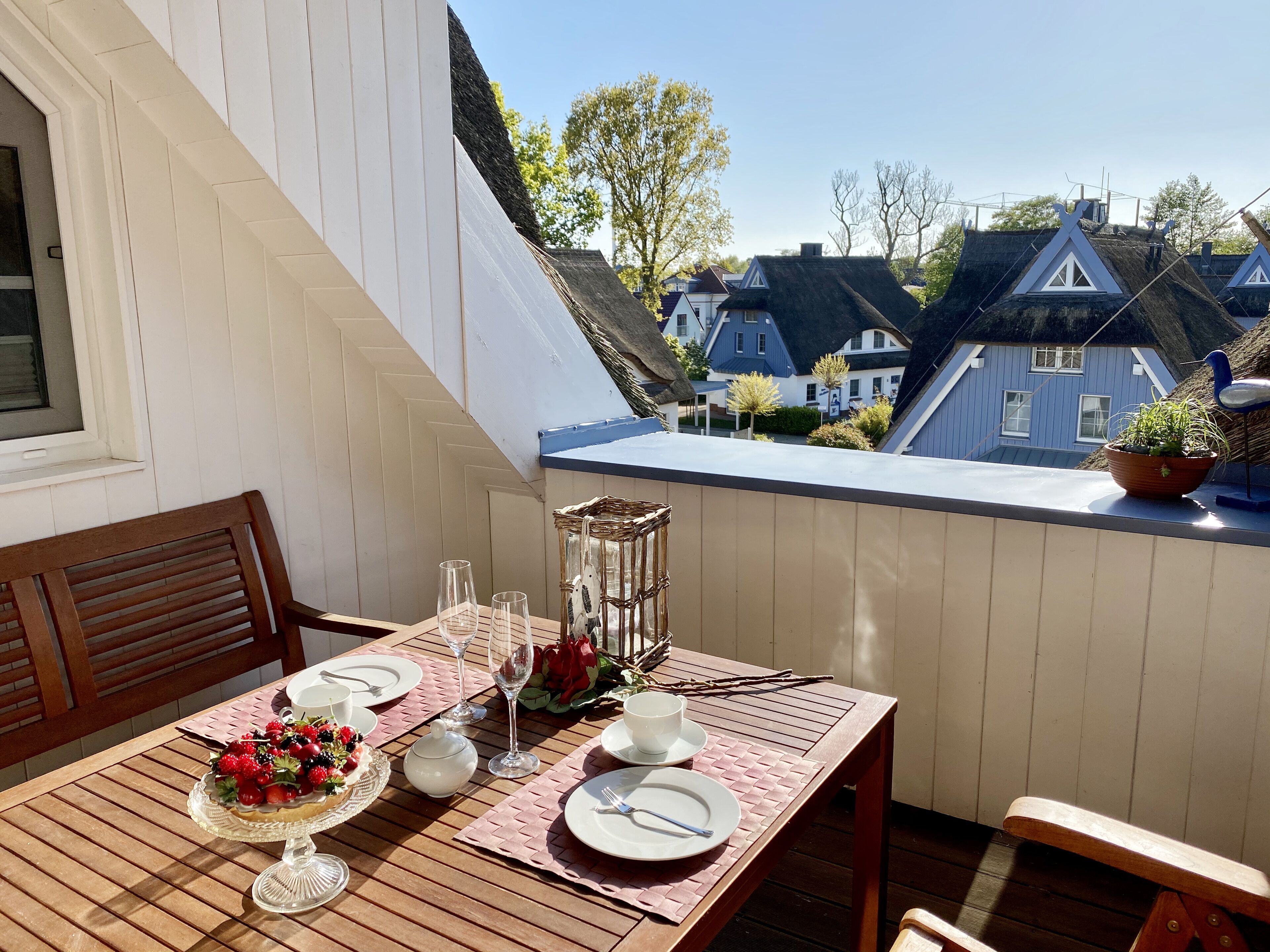 A dining table set on a balcony with a view of houses.