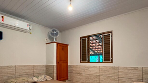 A bedroom with a bed, a wardrobe, a window with shutters, and an air conditioning unit. - CHALÉS BONSUCESSO (Pirenópolis)