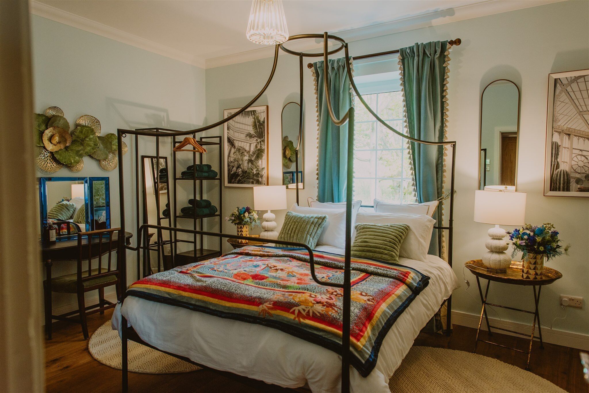 A four-poster bed with a colorful quilt, a small round table with a lamp, and a chair.