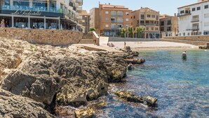 Un hôtel situé sur la côte, avec une plage rocheuse, une eau d’un bleu limpide et différents bâtiments, dont un restaurant.
