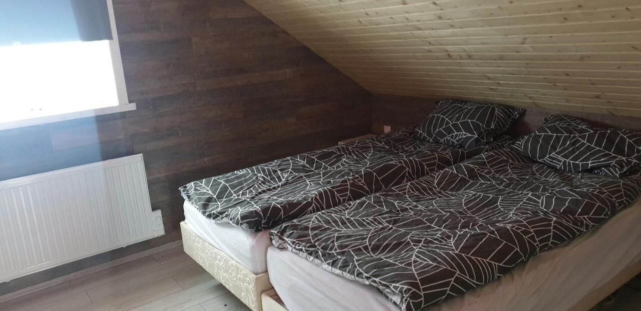 Una habitación pequeña y acogedora con techo inclinado y paredes de madera. Tiene una cama individual con colcha estampada y dos almohadas. Se observa un radiador en el lado izquierdo de la habitación.