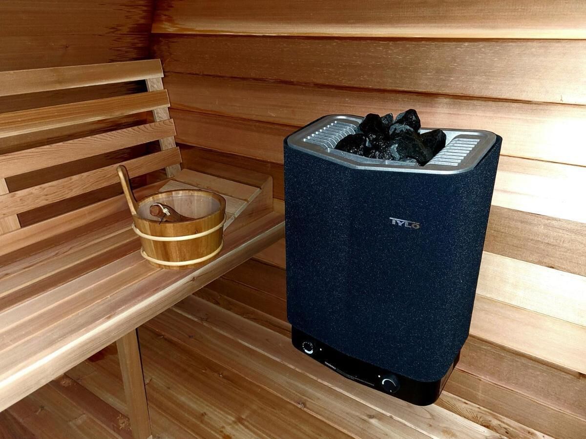 A sauna with a wooden bench and a metal container holding stones.