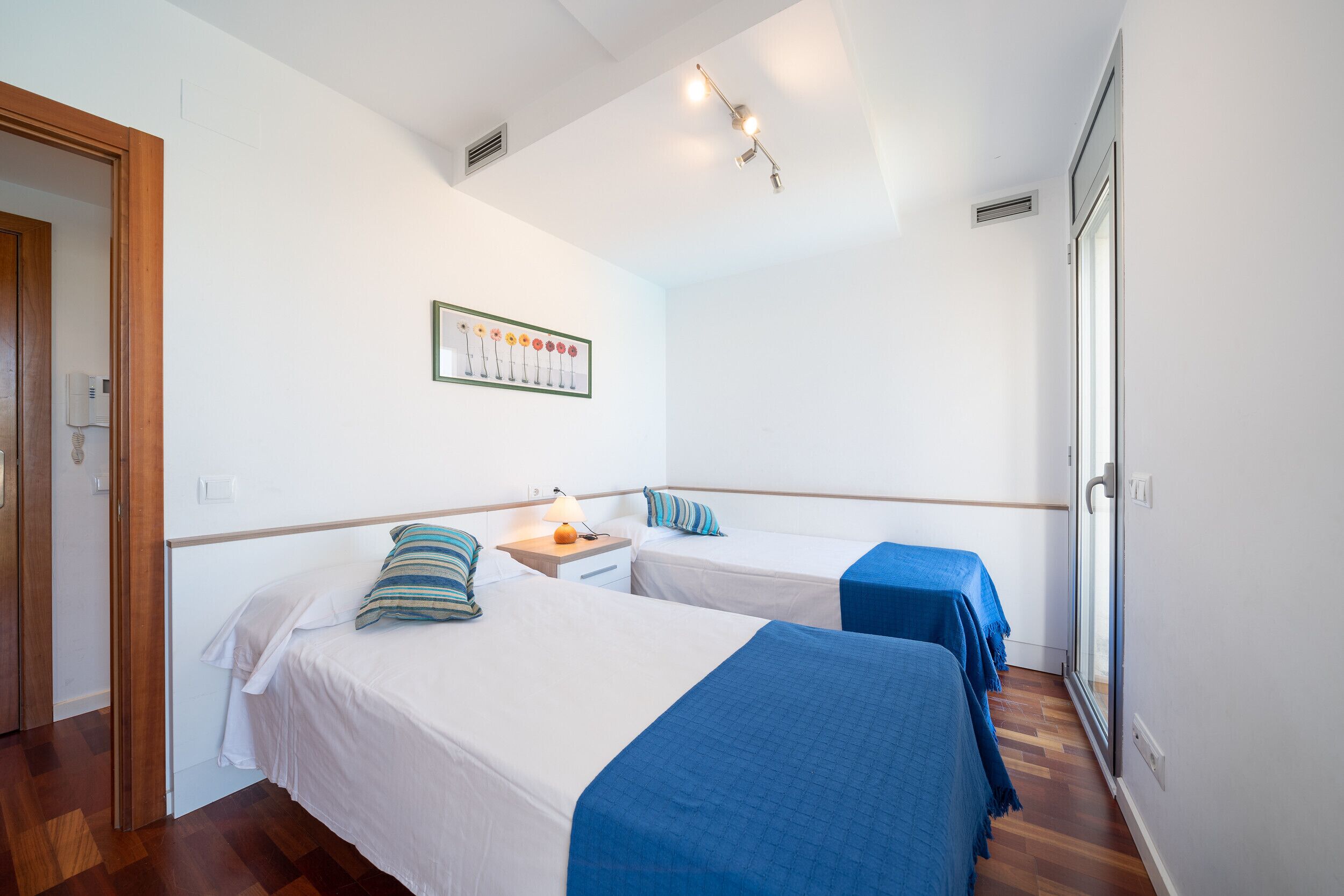 A hotel room with two beds, a wooden door, a framed picture on the wall, and a window with a view.