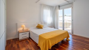 Quarto com cama, mesa de cabeceira, abajur, manta amarela e uma grande porta de vidro deslizante que dá para uma área externa.