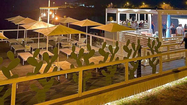 An outdoor seating area with tables and umbrellas, a cactus decoration, and a building with people in the background. - Housing of Charme With Rooftops Balconies (Galatone)