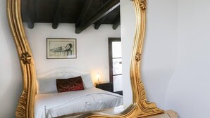 A bedroom with a bed, a nightstand, a lamp, a framed picture on the wall, and a large ornate mirror. - Housing of Charme With Rooftops Balconies (Galatone)