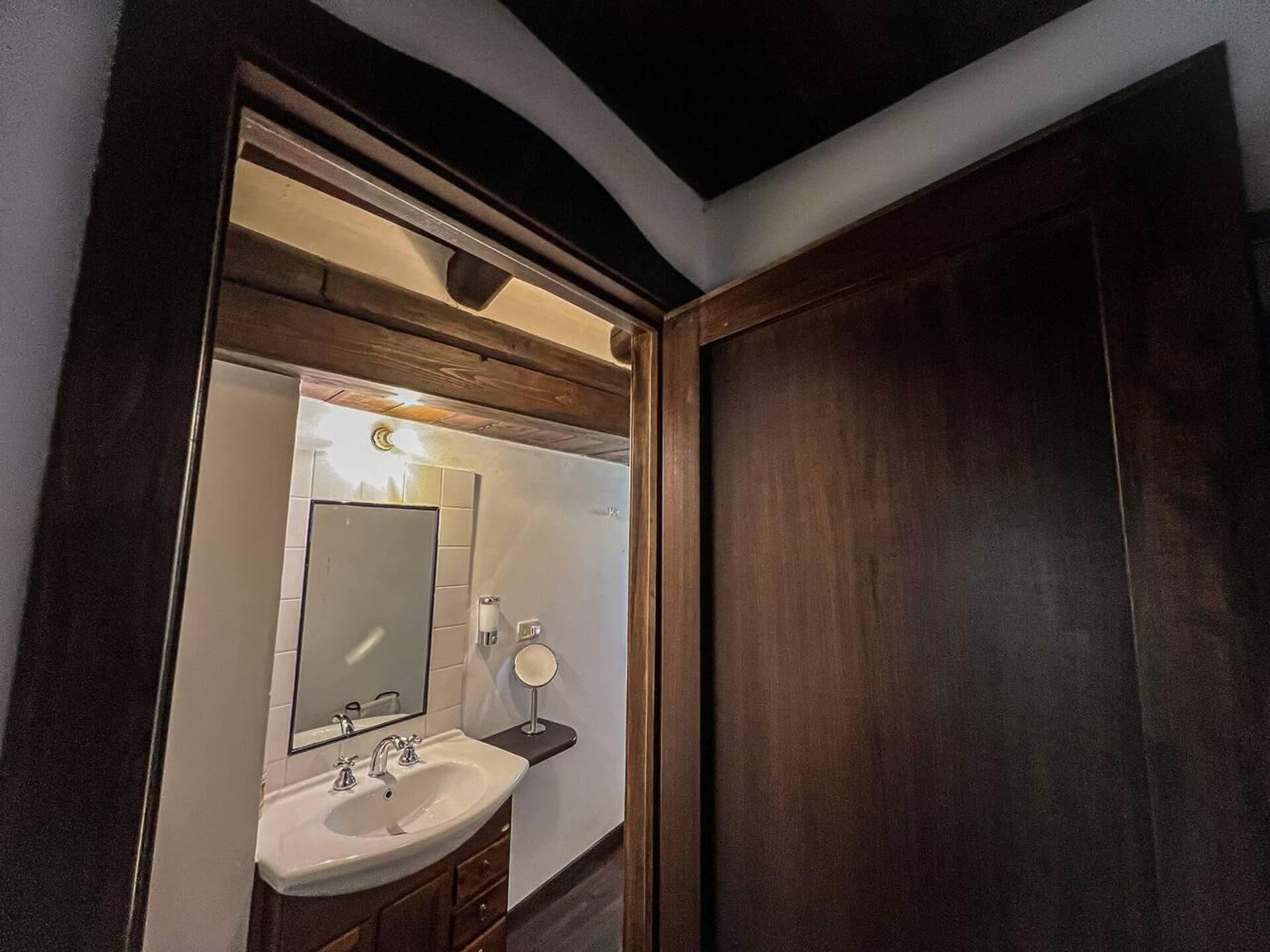 Une salle de bain avec un grand miroir, un lavabo et un petit miroir rond posé sur une étagère.