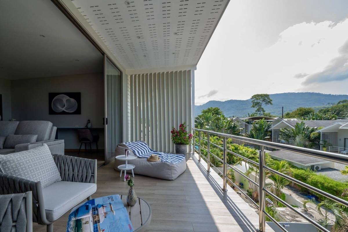 A modern balcony with a sofa, a small table, and a view of a lush landscape with mountains.