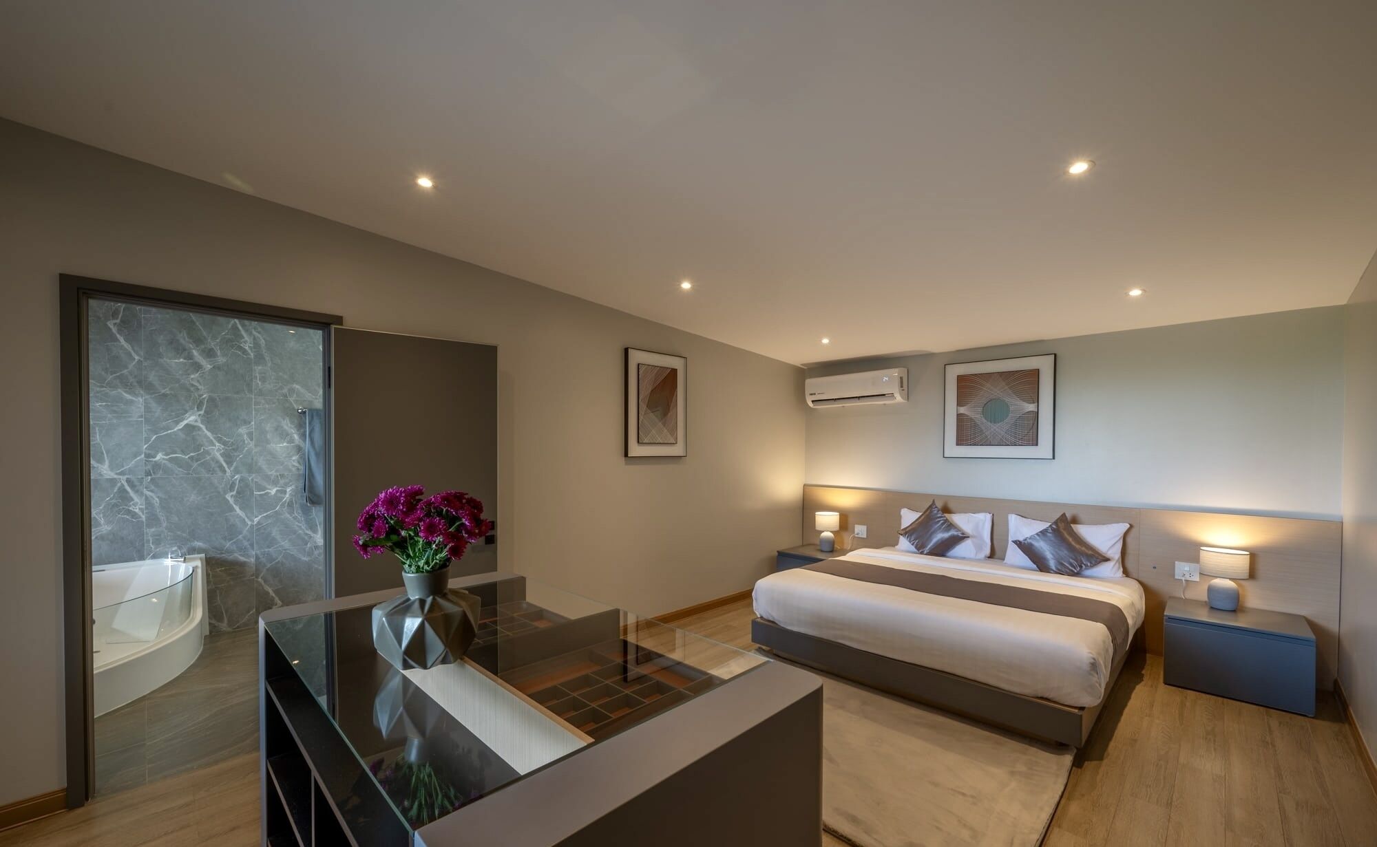 A modern bedroom with a bed, bedside tables, a glass coffee table, and a bathroom with a glass shower enclosure.