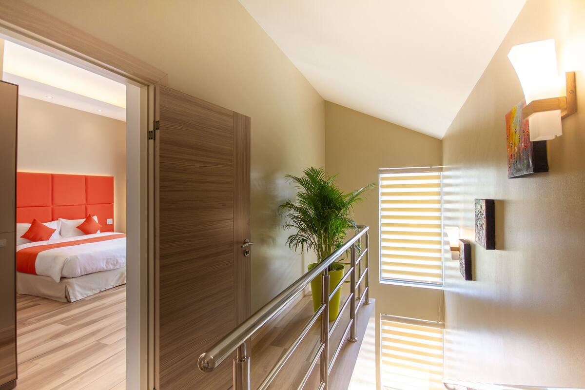 A hotel room with a bed, a plant, and a staircase.