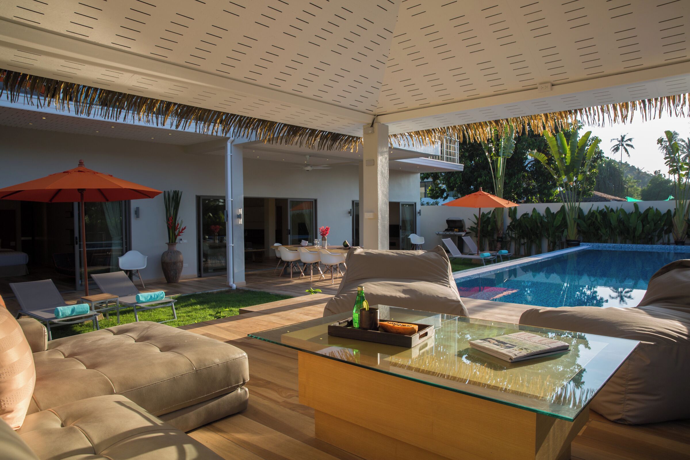 Un espace de vie extérieur moderne avec une table basse en verre, des canapés de couleur beige et une piscine.