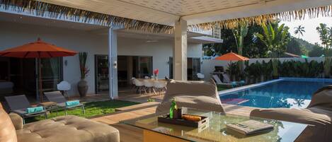 Un espace de vie extérieur moderne avec une table basse en verre, des canapés de couleur beige et une piscine.