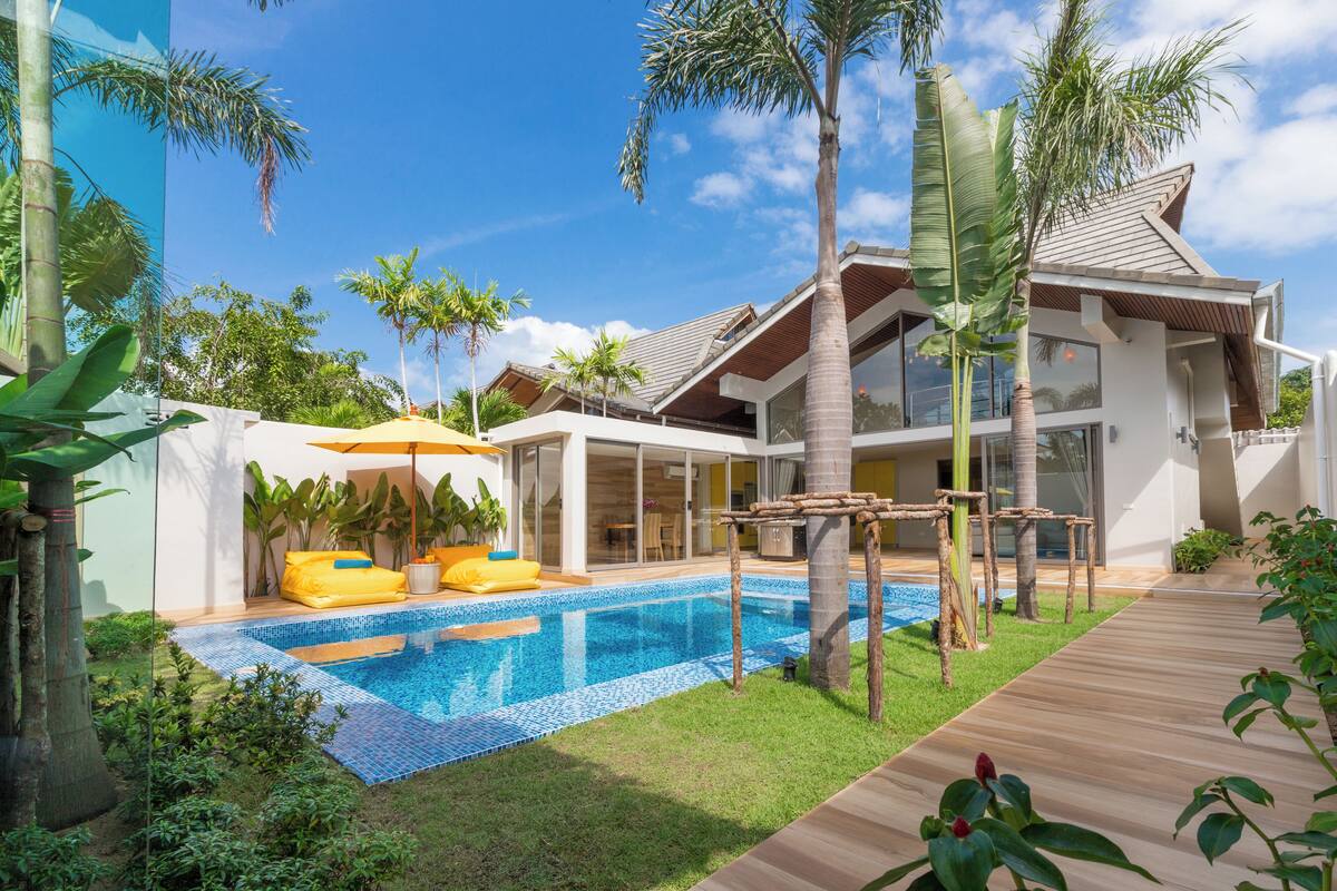 A modern house with a swimming pool, wooden deck, and tropical plants.