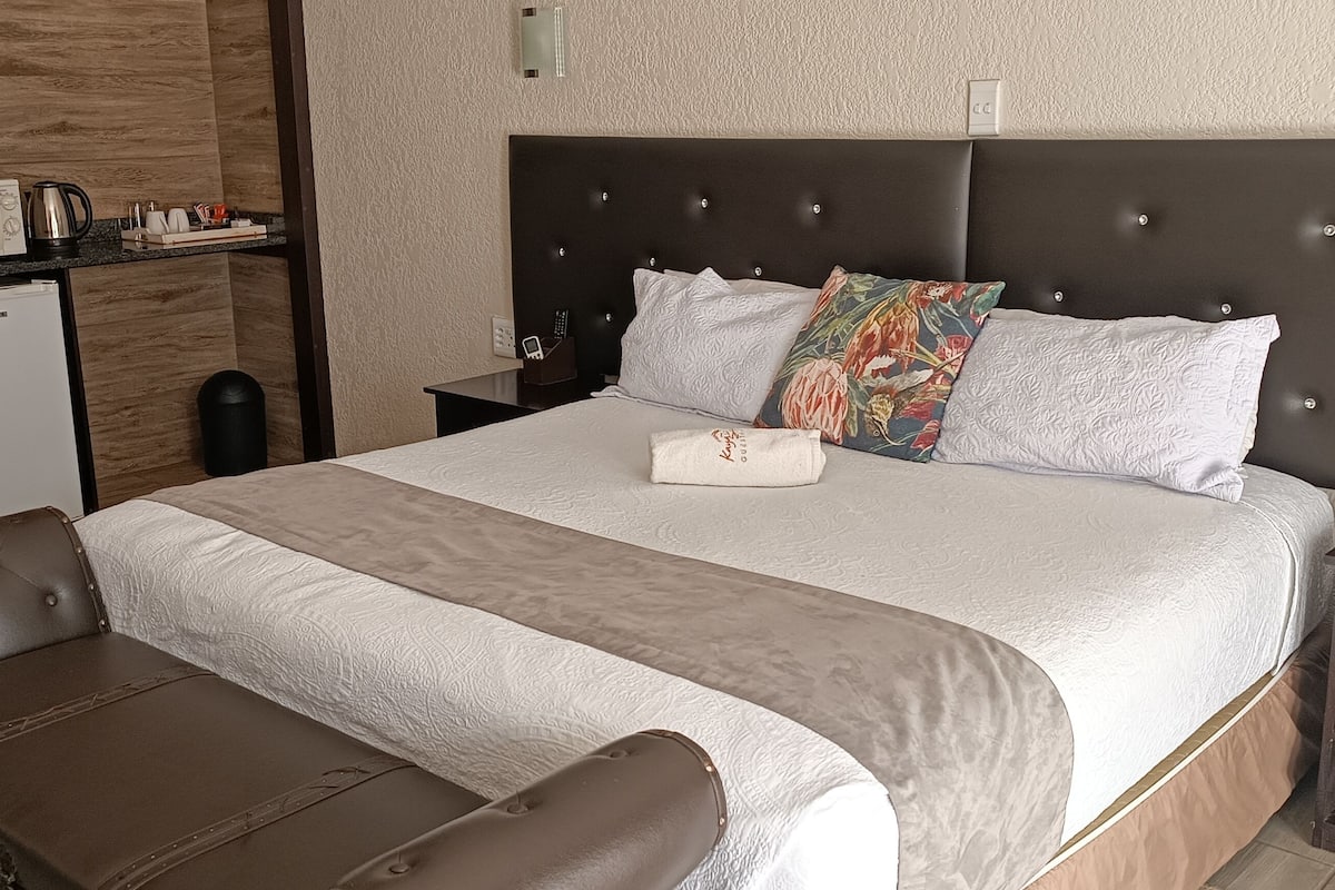 Een hotelkamer met een bed, nachtkastje, bureau, stoel, magnetron, koelkast en prullenbak.