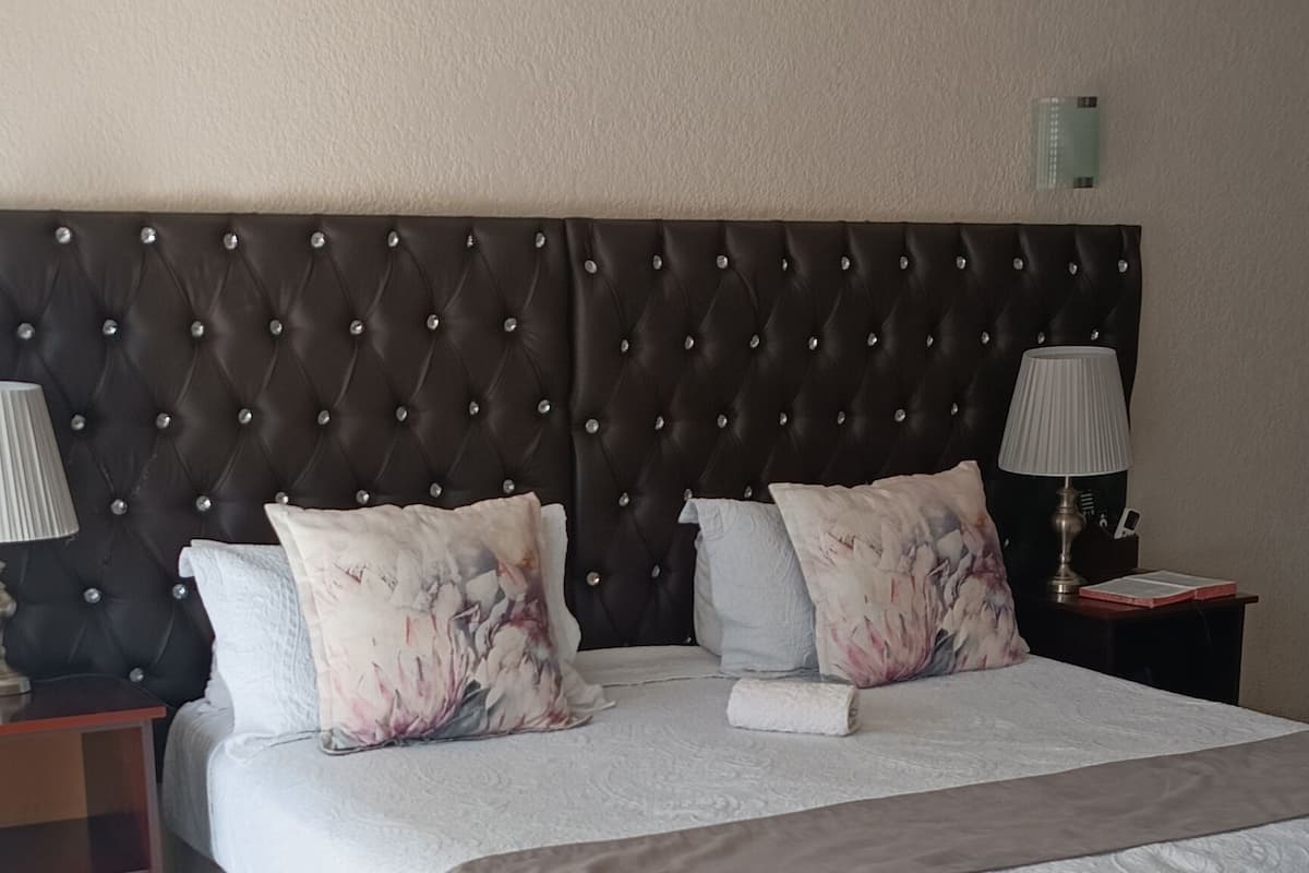 Een slaapkamer met een groot bed, een nachtkastje, een lamp en een wandairconditioner.