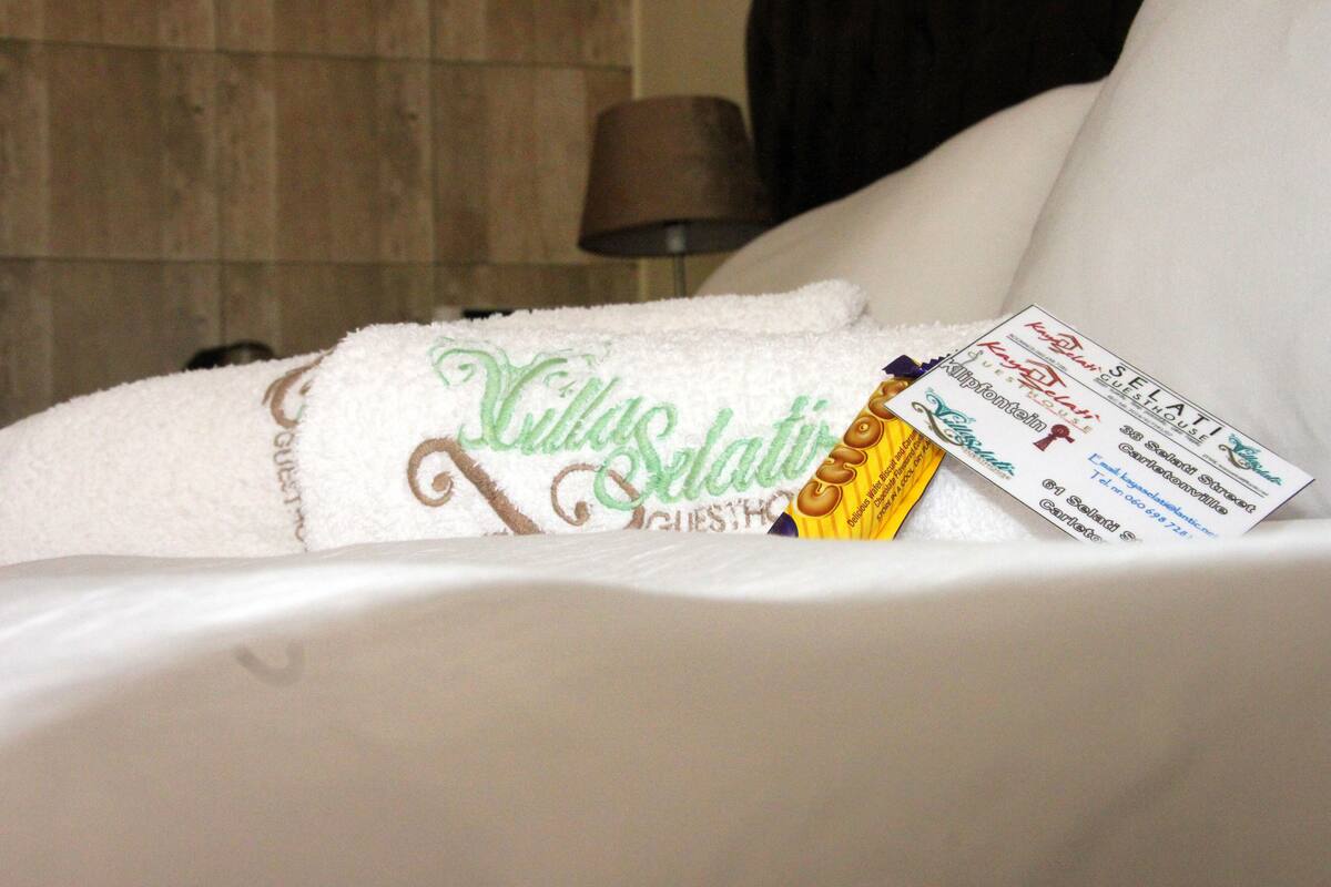 Een hotelkamer met een wit bed, een handdoek met 'Villa Selat' geborduurd erop, en een kaartje op het bed.