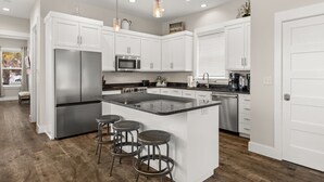 A modern kitchen with white cabinets, stainless steel appliances, a central island with stools, and pendant lighting.