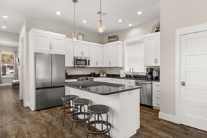 A modern kitchen with white cabinets, stainless steel appliances, a central island with stools, and pendant lighting.
