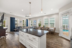 A spacious living area with a central island, a dining table, and a view of a pool.