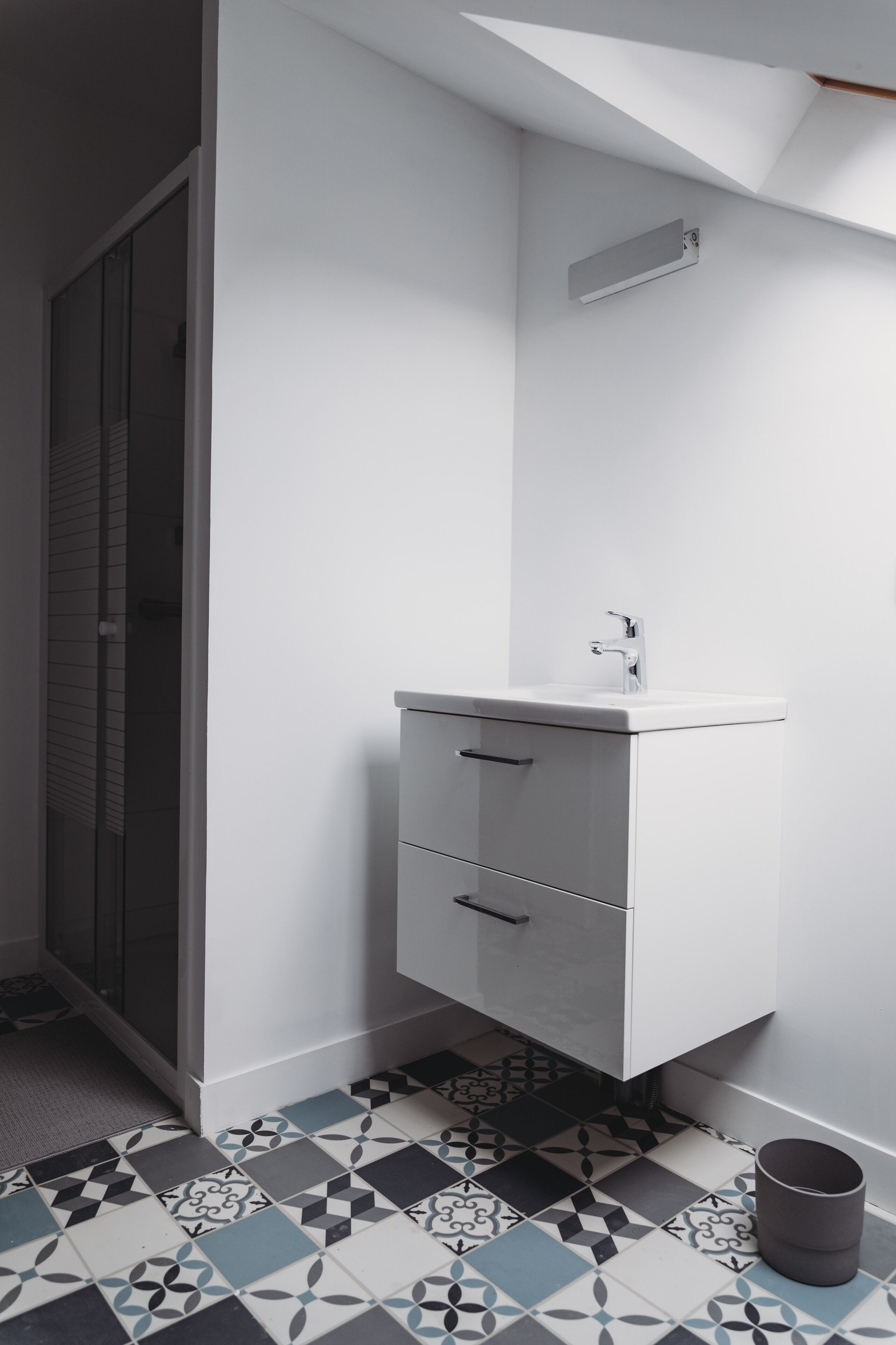 Une salle de bain avec un lavabo blanc, un miroir et des carreaux de sol à motifs.