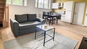 A modern living room with a grey sofa, a glass coffee table, and a dining area with a table and chairs.