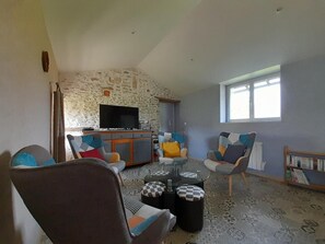 A living room with a stone wall, a flat-screen TV, a coffee table, and two armchairs with patterned cushions.