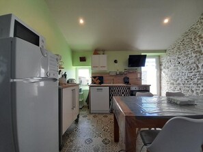 Una cocina compacta con refrigerador, microondas y una pequeña isla con pileta. Hay un televisor montado en la pared y una ventana que proporciona luz natural.
