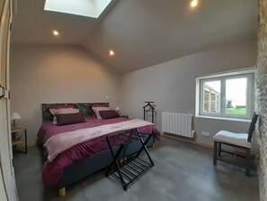 Un dormitorio con cama, una silla, un radiador, un ventanal y un tragaluz.