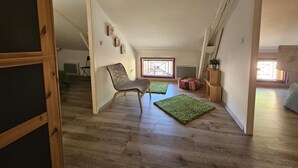 A loft-style room with a high ceiling, wooden flooring, a green rug, a chair, and a window with a view. - Gîte du Séchoir - Bouresse (BOURESSE)