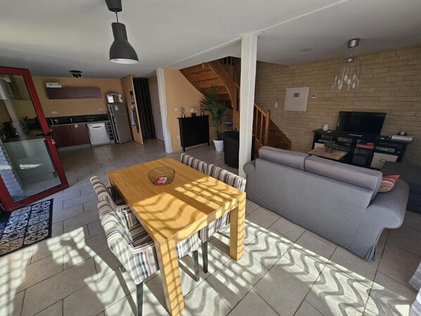 A modern living space with a dining area, sofa, TV, kitchen, and staircase.