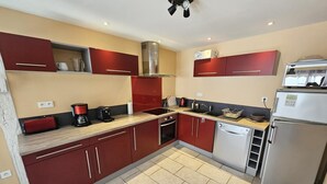 A modern kitchen with red cabinets, a stainless steel range hood, a built-in dishwasher, and a refrigerator. - Gîte du Séchoir - Bouresse (BOURESSE)