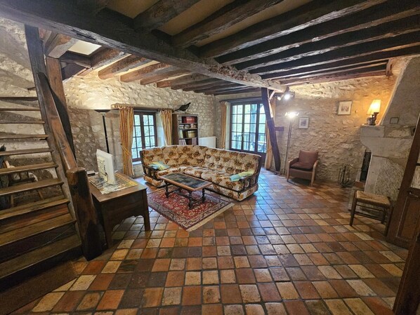 A rustic room with a stone wall, wooden beams, a sofa, a table, and a chair.