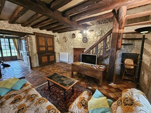 A rustic room with a wooden staircase, a television on a wooden table, a sofa with patterned cushions, and a stone wall.