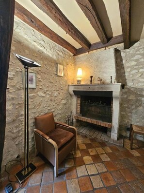 A stone-walled room with a fireplace, a leather armchair, and a floor lamp.