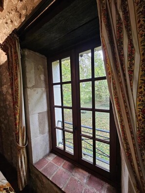 A window with a view of a garden, a stone wall, and a wooden beam above.